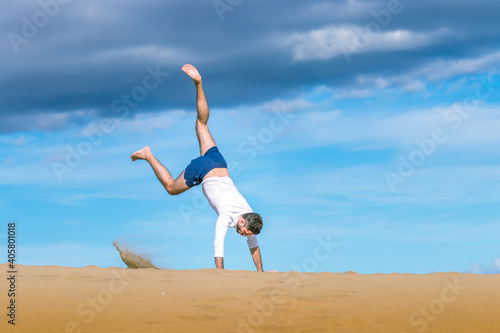 Athletic young man doing acrobatics in the sand of the dunes in Gran Canaria