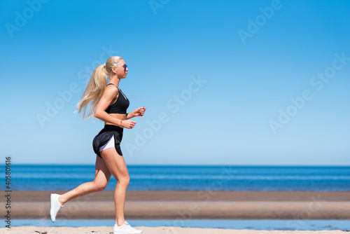 Outdoor sports. A blonde sportswoman in summer sportswear runs on the beach against the background of the sea.