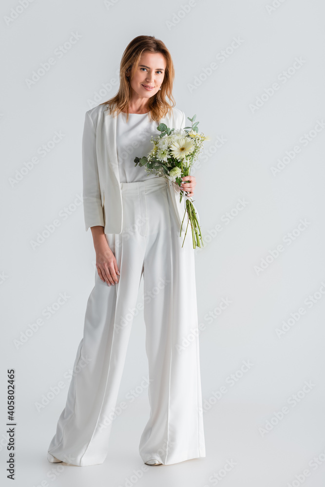 full length of woman in white outfit holding flowers on grey full length of woman in white outfit holding flowers on grey