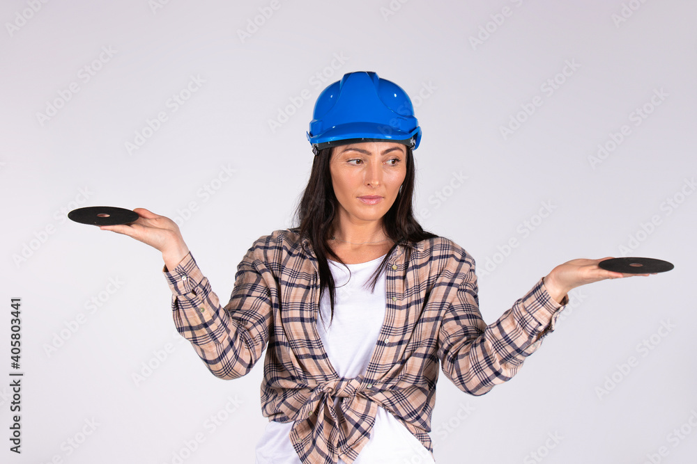 A woman in a hard hat with outstretched arms looks to the side and holds abrasive disks on a white background. A woman in a hard hat with outstretched arms looks to the side and holds abrasive disks on a white background.