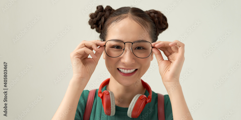 Cute female student touching glasses, posing over white wall