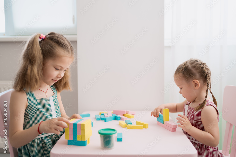 Fototapeta premium Lovely kids plaing with colorful wodden blocks in a creative educational game as they stand at a pink table