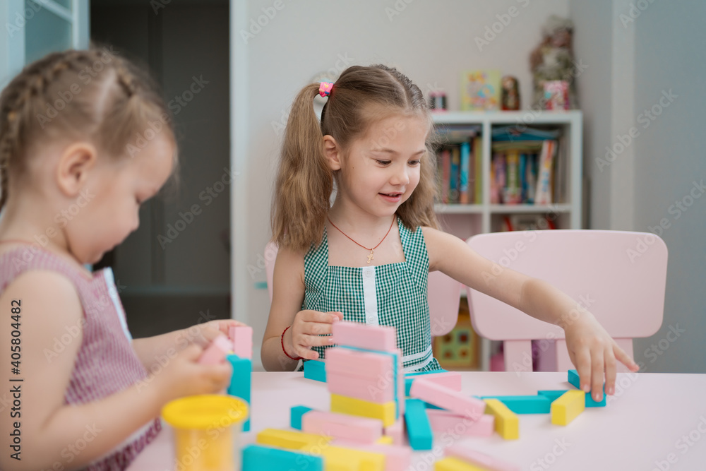 Lovely kids plaing with colorful wodden blocks in a creative educational game as they stand at a pink table Lovely kids plaing with colorful wodden blocks in a creative educational game as they stand at a pink table