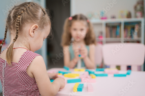 Lovely kids plaing with colorful wodden blocks in a creative educational game as they stand at a pink table