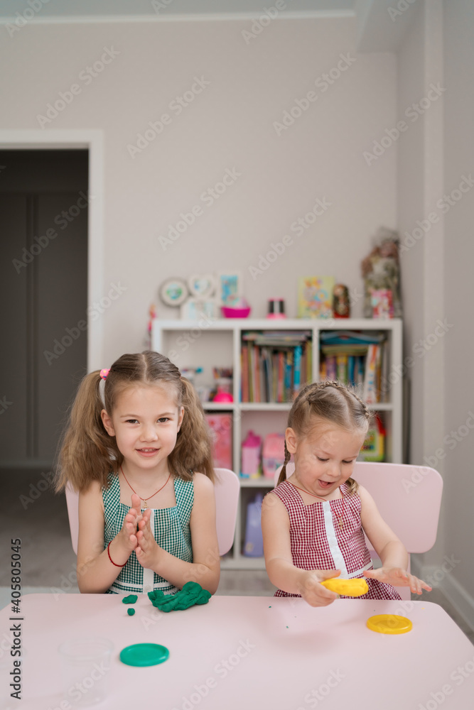 Naklejka premium Little girls with lovely faces play with clay molding shapes, learning through playing with colored plasticine developing creativity