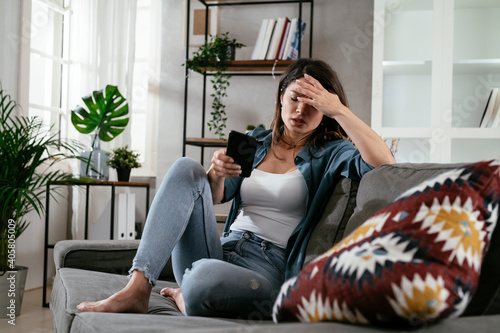 Sad woman sitting on the couch, using the phone. Upset woman waiting for a phone call...