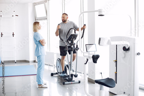 A woman is a physiotherapist. A man is using a spin bike. The patient is having a treatment. photo