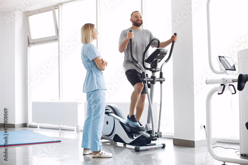 A woman is a physiotherapist. A man is using a spin bike. The patient is having a treatment. photo
