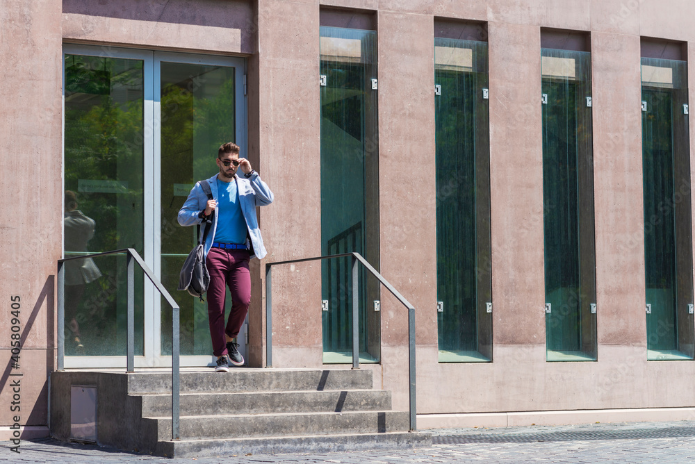 Young businessman walking next to office buildings while holding a shoulder bag outdoors