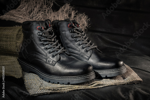 Black boots made of genuine leather. Men's winter shoes with laces, fashionable style. On a dark leather background.
