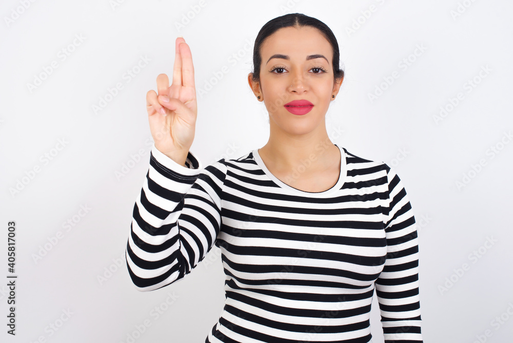 Young beautiful woman wearing stripped t-shirt against white background pointing up with fingers number ten in Chinese sign language Shi Young beautiful woman wearing stripped t-shirt against white background pointing up with fingers number ten in Chinese sign language Shi
