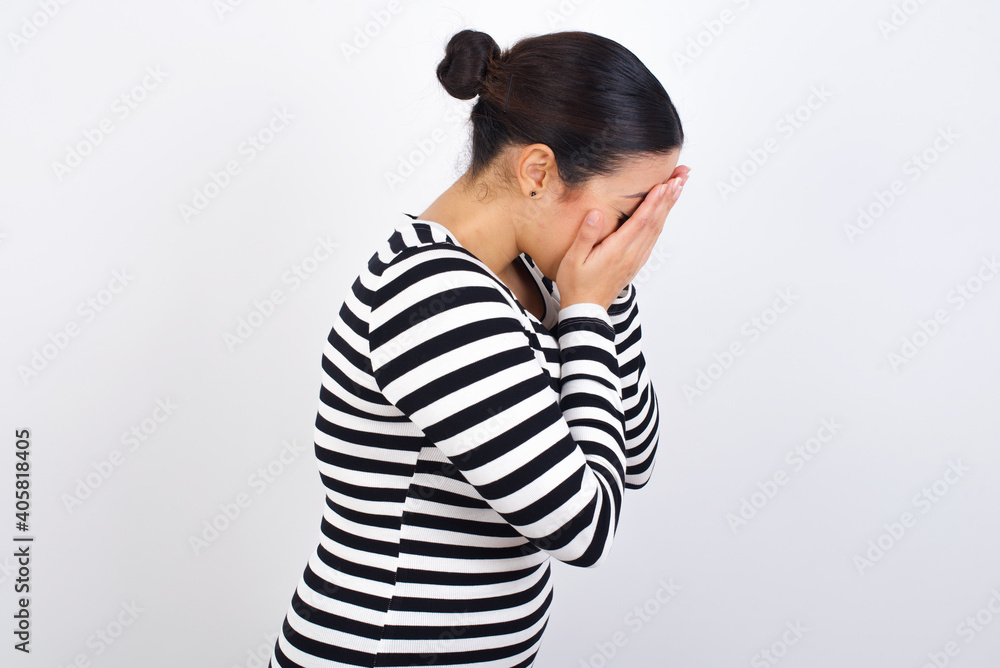 Sad Young beautiful woman wearing stripped t-shirt against white background crying covering her face with her hands. Sad Young beautiful woman wearing stripped t-shirt against white background crying covering her face with her hands.