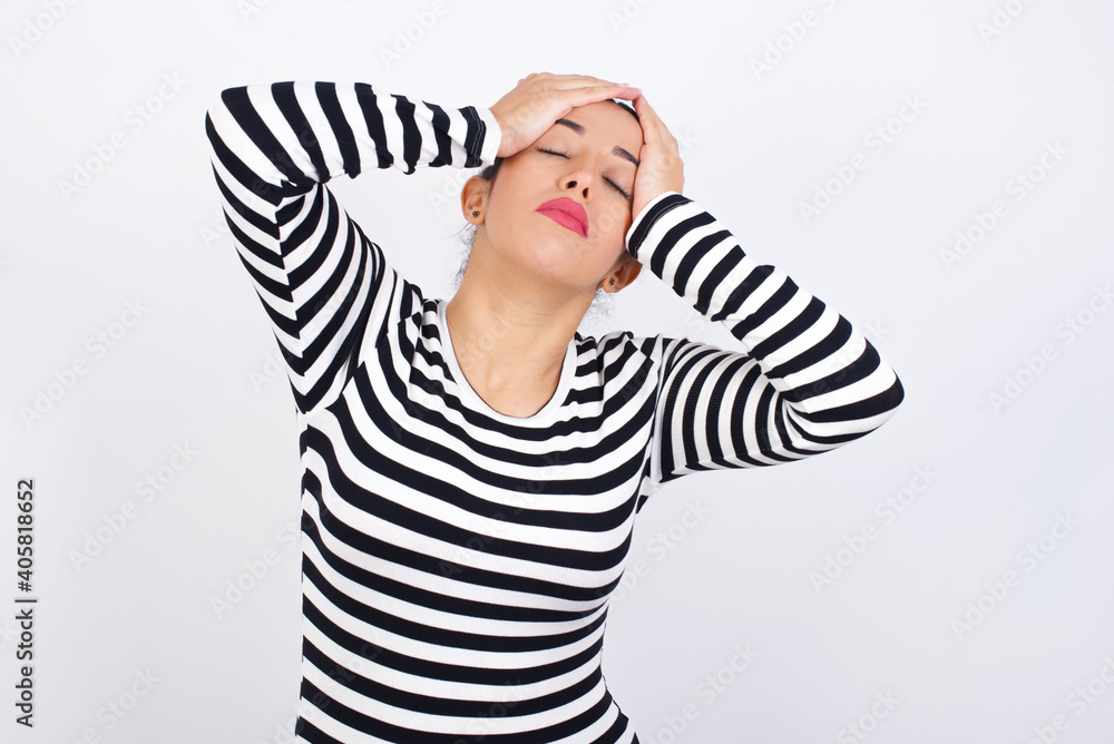 Young beautiful woman wearing stripped t-shirt against white background suffering from strong headache desperate and stressed because of overwork. Depression and pain concept. Young beautiful woman wearing stripped t-shirt against white background suffering from strong headache desperate and stressed because of overwork. Depression and pain concept.