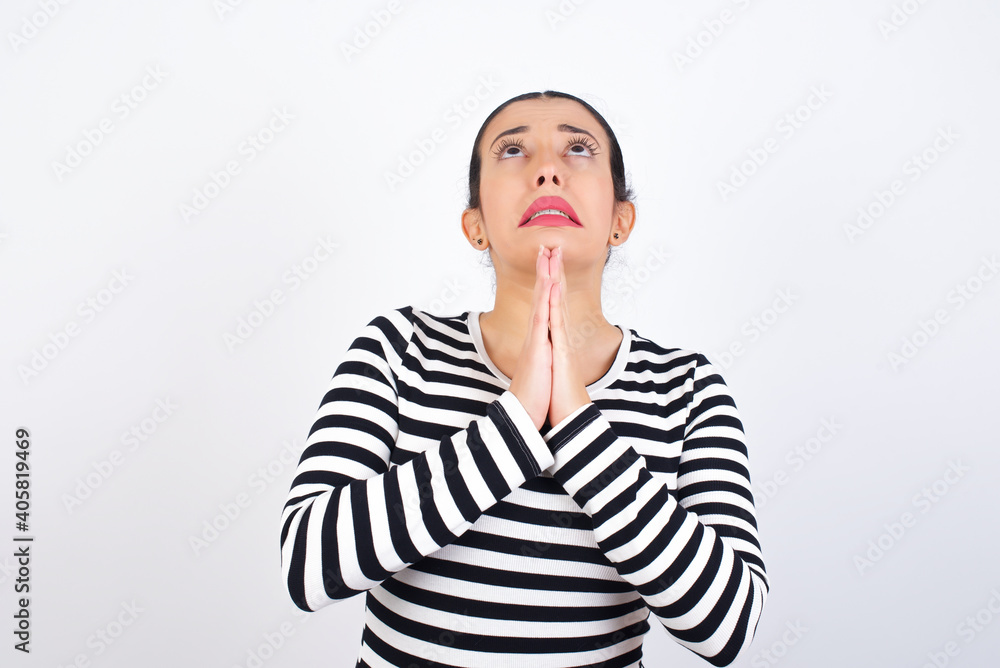Young beautiful woman wearing stripped t-shirt against white background begging and praying with hands together with hope expression on face very emotional and worried. Please God Young beautiful woman wearing stripped t-shirt against white background begging and praying with hands together with hope expression on face very emotional and worried. Please God