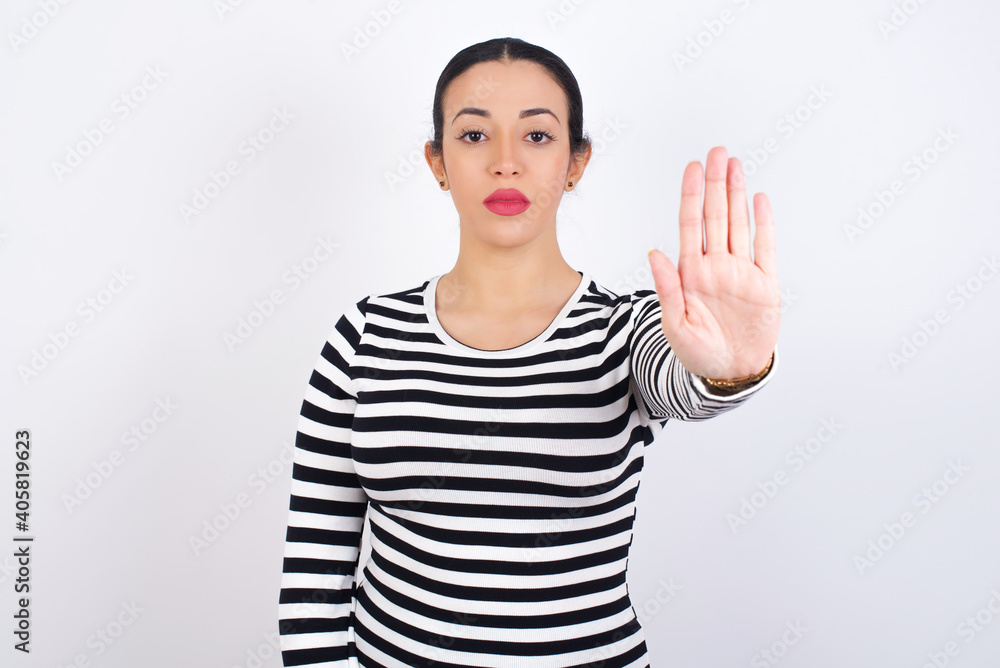 Young beautiful woman wearing stripped t-shirt against white background doing stop sing with palm of the hand. Warning expression with negative and serious gesture on the face. Young beautiful woman wearing stripped t-shirt against white background doing stop sing with palm of the hand. Warning expression with negative and serious gesture on the face.