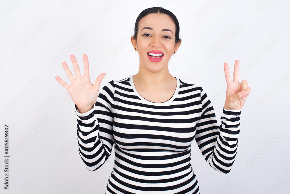 Young beautiful woman wearing stripped t-shirt against white background showing and pointing up with fingers number seven while smiling confident and happy. Young beautiful woman wearing stripped t-shirt against white background showing and pointing up with fingers number seven while smiling confident and happy.
