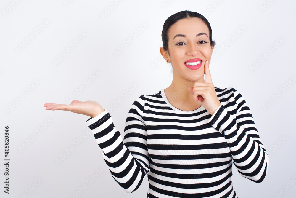 Funny Young beautiful woman wearing stripped t-shirt against white background holding open palm new product. I wanna buy it! Funny Young beautiful woman wearing stripped t-shirt against white background holding open palm new product. I wanna buy it!