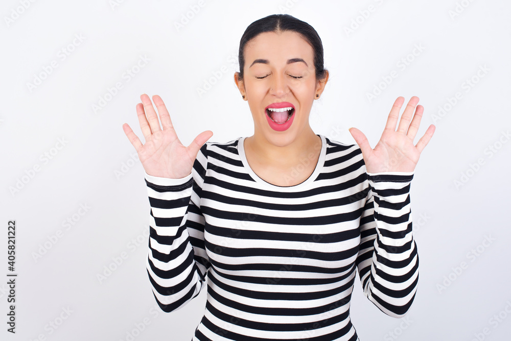 Emotive Young beautiful woman wearing stripped t-shirt against white background laughs loudly, hears funny joke or story, raises palms with satisfaction, being overjoyed amused by friend Emotive Young beautiful woman wearing stripped t-shirt against white background laughs loudly, hears funny joke or story, raises palms with satisfaction, being overjoyed amused by friend