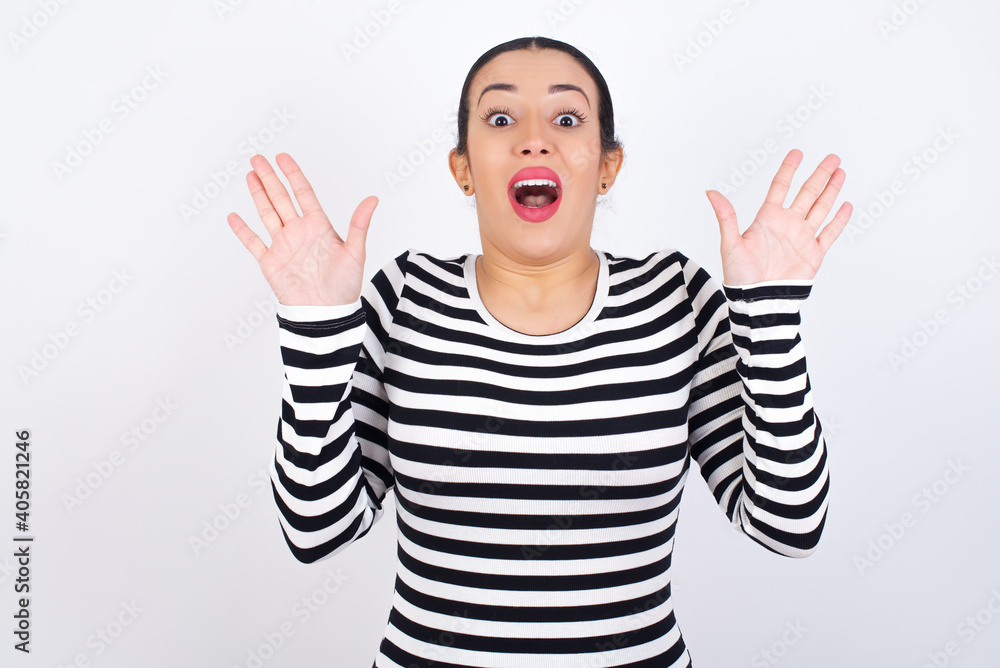 Naklejka premium Optimistic Young beautiful woman wearing stripped t-shirt against white background raises palms from joy, happy to receive awesome present from someone, shouts loudly, Excited model screaming.
