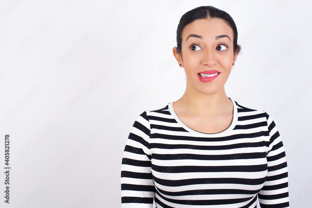 Amazed Young beautiful woman wearing stripped t-shirt against white background bitting lip and looking tricky to empty space. Amazed Young beautiful woman wearing stripped t-shirt against white background bitting lip and looking tricky to empty space.