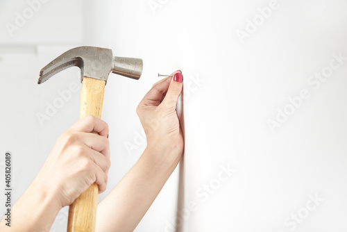 Картината върху платно Young woman with manicured hands nailing a nail into a white wall