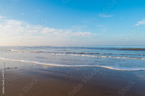 Fototapeta Naklejka Na Ścianę i Meble -  relaxing and gentle calming waves flowing into a beach at sundown, with a vivid blue sky and reflection. calming fresh air walks into nature during corona virus lockdowns