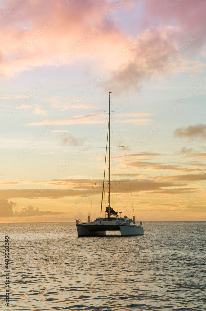 Anchoring ship in tropical bay at sunset. Small yacht and catamaran on sea water during dusk. Santa Lucia. Caribbean lifestyle themes.