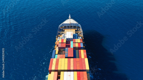 Aerial drone photo of industrial colourful vessel carrying heavy truck size containers cruising the Aegean deep blue sea