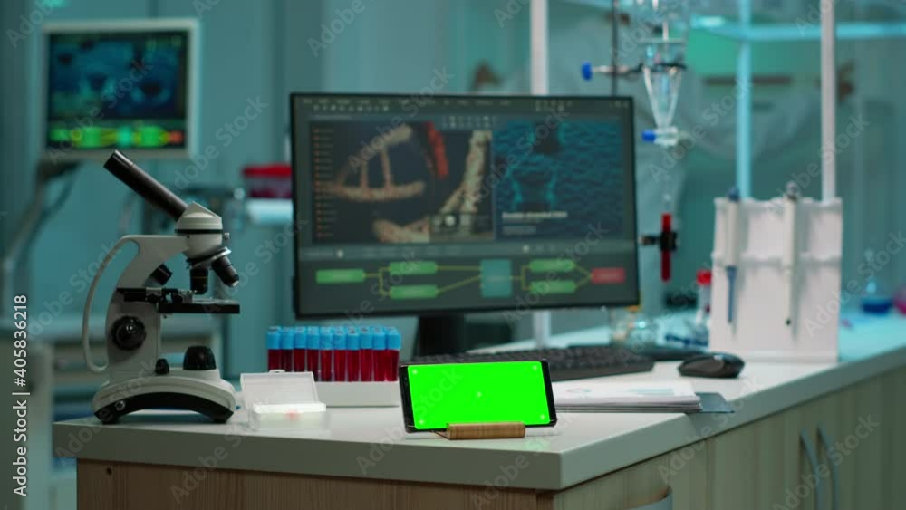 Scientist standing at monitor in background analysing virus evolution while phone with mock-up green screen working in front. Woman lab researcher examining vaccine developent bringing blood samples Scientist standing at monitor in background analysing virus evolution while phone with mock-up green screen working in front. Woman lab researcher examining vaccine developent bringing blood samples