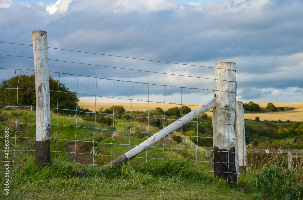 A wire fence with wooden pales around fields.