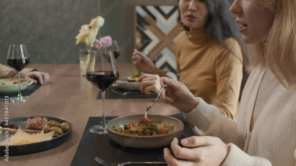 Slow-motion close-up of young pretty multi-ethnic women having dinner in modern restaurant talking and eating beautiful meals Slow-motion close-up of young pretty multi-ethnic women having dinner in modern restaurant talking and eating beautiful meals