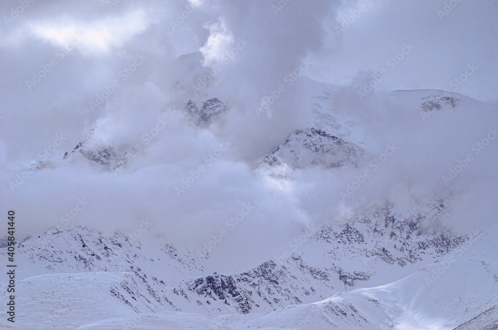 panoramic view of snowcapped mountain summits between morning clouds on blue sky background