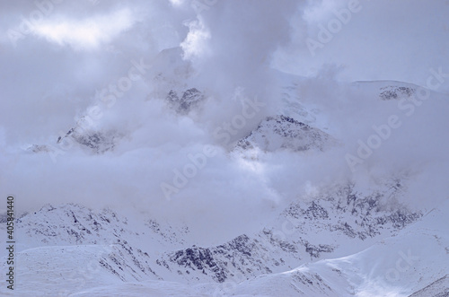 panoramic view of snowcapped mountain summits between morning clouds on blue sky background