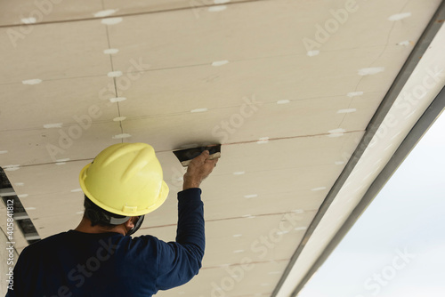 Valokuva A man applies putty to gypsum roof overhang of a commercial building