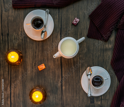 Top view of a two-person set of espresso coffee with white cups and milk jug with yellow candles on wooden background