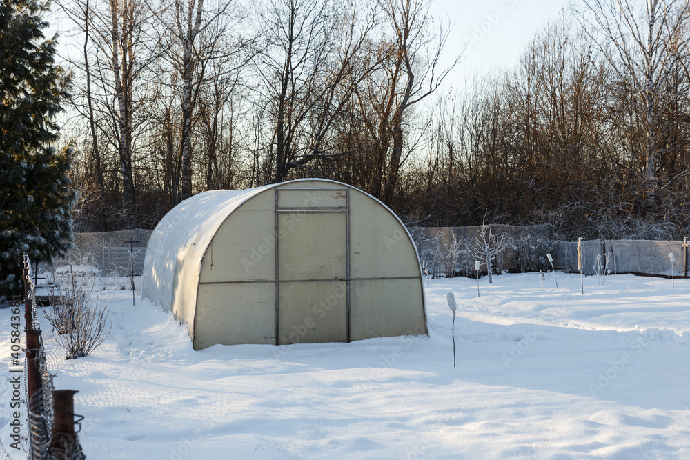 Greenhouse in the vegetable garden in winter. Small greenhouse with a metal frame covered with polycarbonate. Greenhouse in the vegetable garden in winter. Small greenhouse with a metal frame covered with polycarbonate.
