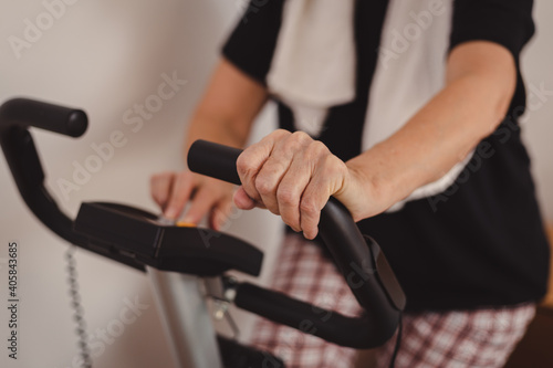 Senior woman in mid 70's exercise on stationary bike at home. Active mature female checking parameters during cycling workout.