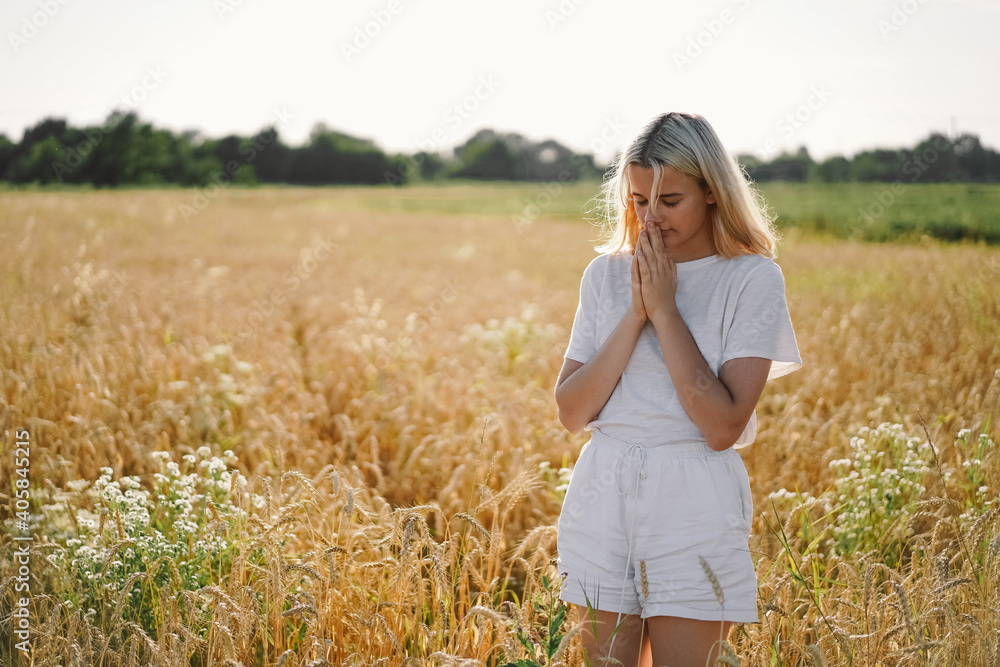Girl closed her eyes, praying in a field. Hands folded in prayer concept for faith Girl closed her eyes, praying in a field. Hands folded in prayer concept for faith