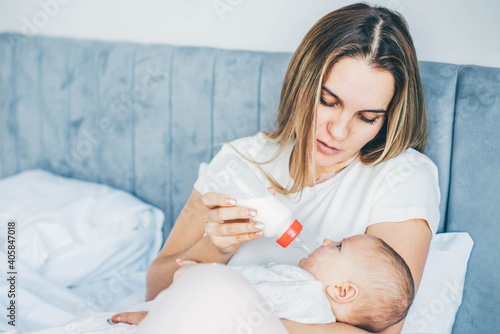 Mother feeding a newborn baby from bottle at home.