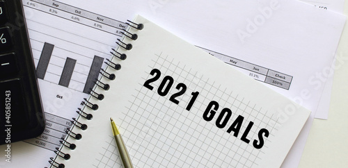 Text 2021 GOALS on the page of a notepad lying on financial charts on the office desk.