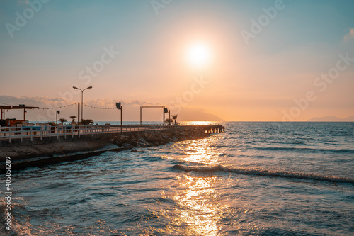 Sunset over the Mediterannean sea. Beautiful landscape of sandy beach with sea waves and wooden pier during sunset. Sky reflections in water.