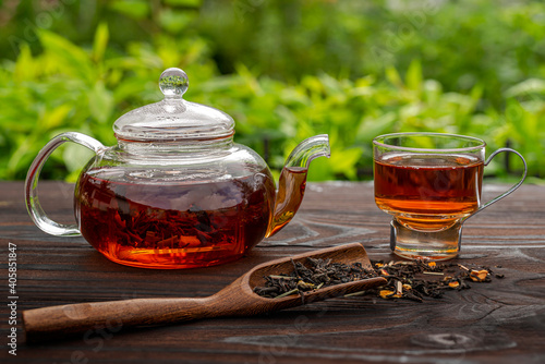 Steamed glass teapot, elegant cup. Bamboo spoon with tea, wooden table. Outdoor, picnic, brunch. Floral background in blur. © TSViPhoto