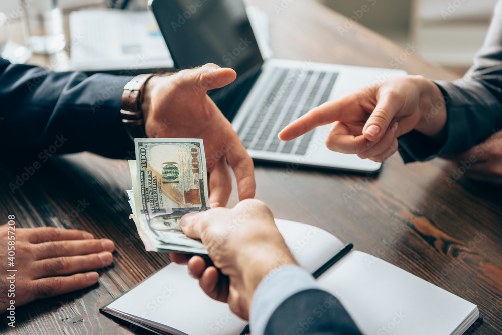 Cropped view of businesswoman pointing at money near businessmen on blurred foreground Cropped view of businesswoman pointing at money near businessmen on blurred foreground