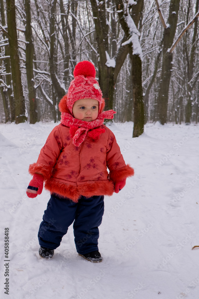 Baby girl in red jacket walking by snow in the forest. Baby girl in red jacket walking by snow in the forest.