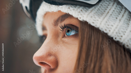 Girl with a white hat and snowboard mask in the forest in winter. Side view. Macro eyes
