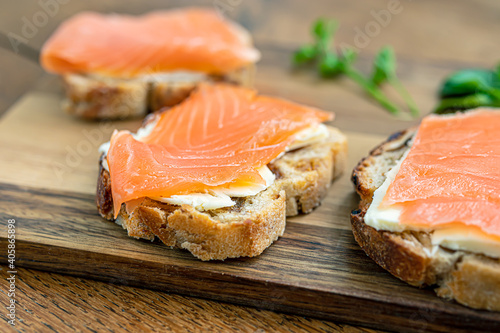 Healthy food, toasts of fig bread with cream cheese and smoked salmon on wooden cutting board close up selective focus