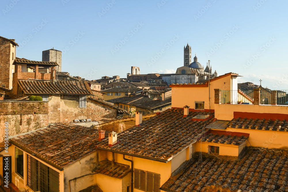 Rooftops view of the historic centre of Siena with the Cathedral in the background against clear blue sky, Tuscany, Italy