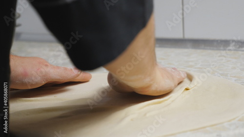 Close up male arms of cook forming pastry on a wooden surface at cuisine. Hands of chef shaping floured dough for pizza on a kitchen table at restaurant. Concept of preparing food. Slow motion