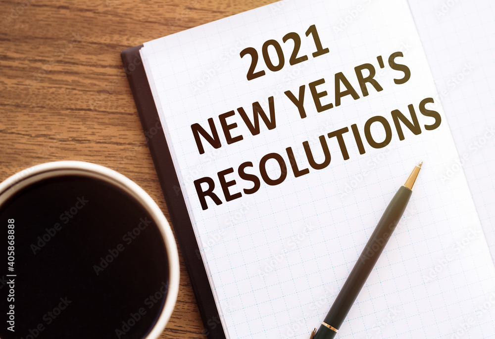 2021 NEW YEAR'S RESOLUTIONS text on notepad on wooden desk. 2021 NEW YEAR'S RESOLUTIONS text on notepad on wooden desk.