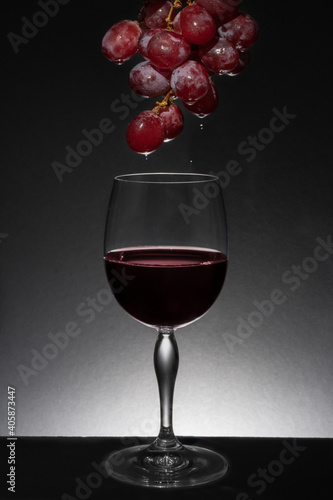 Copa de cristal con uvas goteando vino en ella. Goteo de vino en copa de cristal sobre fondo y base negra. Iluminación posterior y superior con spot.